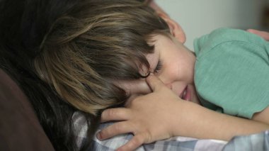 Üzgün, ağlayan küçük bir çocuk. Anne omzuna yaslanan çocuk yorgun ve mutsuz hissediyor.