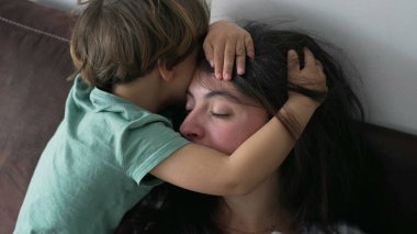 Çocuğu kucaklayan anne. Samimi küçük çocuk annesinin kafasına sarılıyor. Sevgi ve şefkat gösteren ebeveyn yüzünü örten çocuk. Özgün aile bakımı