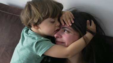 Çocuğu kucaklayan anne. Samimi küçük çocuk annesinin kafasına sarılıyor. Sevgi ve şefkat gösteren ebeveyn yüzünü örten çocuk. Özgün aile bakımı