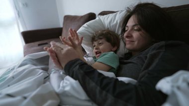 Anne ve çocuk evdeki kanepede yatıyorlar. Anne oğlunu öpüyor, sevgi ve şefkat gösteriyor. Ebeveyn ve çocuk koltukta el çırpıyor.
