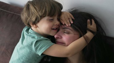 Çocuğu kucaklayan anne. Samimi küçük çocuk annesinin kafasına sarılıyor. Sevgi ve şefkat gösteren ebeveyn yüzünü örten çocuk. Özgün aile bakımı