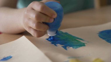 Küçük çocuk elleri kağıt üzerinde boya tüpüne basıyor. Yaratıcılık etkinliği sırasında fırça kullanan çocuk elini kapatır