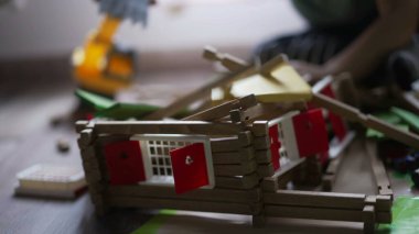 Küçük bir çocuk traktör buldozeriyle tahta ev oyuncağını yok ediyor. Erkek destroyer çocuk odasında oynuyor.