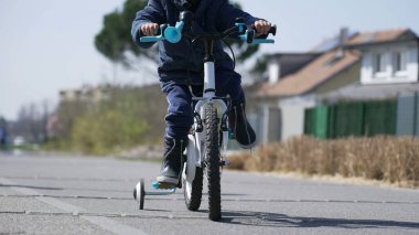 Küçük çocuk kış mevsiminde dışarıda yeşil yolda bisiklet sürmeyi öğreniyor. Çocuk dışarıda bisiklet sürmeyi öğreniyor.