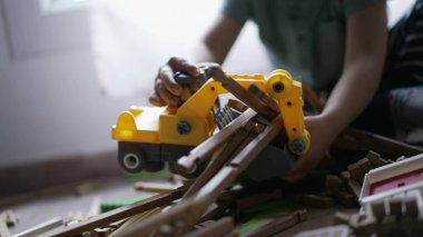 Çocuk buldozer traktör oyuncağıyla oynuyor. Oyun odasında odun topluyor. Kapalı çocuk elleri