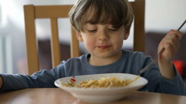 Çatalla makarna yiyen küçük bir çocuk. Çocuk öğle yemeği karbonhidratı yiyor. Çocuk beslenme konsepti