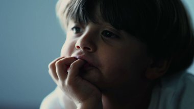 Yüzü çenesinde el olan yakın çocuk yüzü çevrimiçi içerik tarafından hipnotize edilen ekranı izliyor