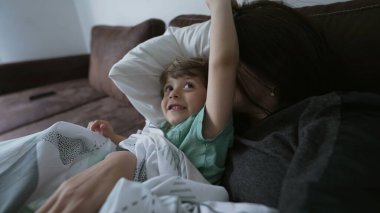 Anne ve çocuk evdeki kanepede yatıyorlar. Anne oğlunu öpüyor, sevgi ve şefkat gösteriyor. Ebeveyn ve çocuk koltukta el çırpıyor.