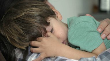 Üzgün, ağlayan küçük bir çocuk. Anne omzuna yaslanan çocuk yorgun ve mutsuz hissediyor.