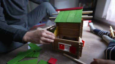 Anne ile aynı odada oynayan çocuk geleneksel tahta ev oyuncağı yapıyor. Küçük çocuk ailesiyle birlikte ev inşa ediyor. 