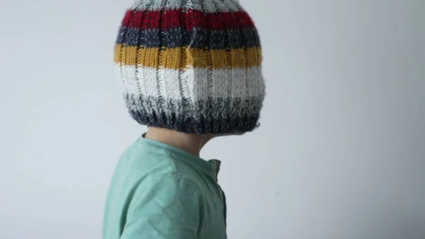 Child face covered with beanie hat. Funny playful little boy blind by knit wool winter accessory