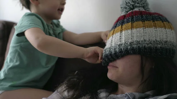 Child putting beanie on mother. Little boy son interacting with mother wearing knit wool winter accessory