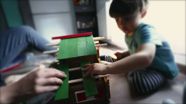 Child building wooden house toy in playroom. One little boy putting wood material on top of house in kid development activity