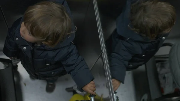 Toddler boy riding elevator going out to play with three wheeled scooter