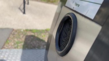 Closeup hand putting glass bottle into recycle dispenser.