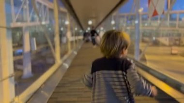 Back of child running at passenger boarding bridge at night. One little boy airplane. Family going for vacation. Kid boarding plane