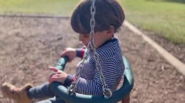 Childhood fun at playground park. Little boy seated inside swing twisting and turning