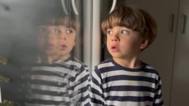 Child sitting by window home pointing outside. One small boy points finger stands by window.