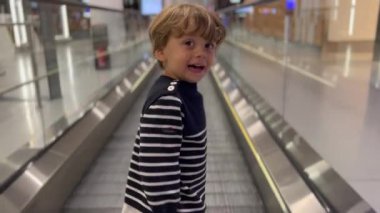 Happy small boy standing on moving corridor at airport terminal. Child traveling concept.