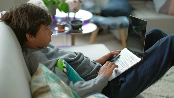 Child browsing internet on laptop computer sitting at sofa
