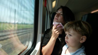 Anne, yürümeye yeni başlayan bebekle sürerken cerrahi maske takıyor.