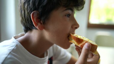 Genç çocuk sabah kahvaltısında reçelli ekmek yiyor.