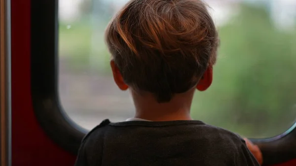 Little boy traveling by train looking outside window