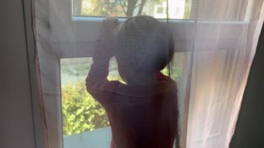 Child standing by window looking through glass. Bored little boy locked inside