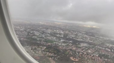 City view seen from up in the air airplane window with clouds. Closeup plane window passenger POV looking down from sky