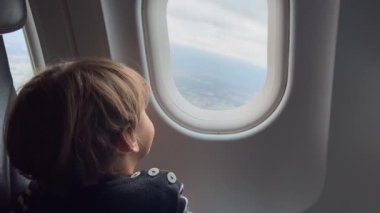 Small child traveling by plane. Little boy staring out airplane window looking at view from above. Travel flight concept