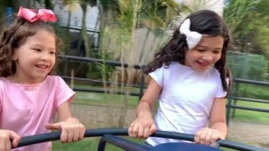 Two little girls playing at playground carousel. Female kids having fun