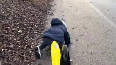 Child falling down in the ground while riding toy scooter. One small boy accident getting hurt