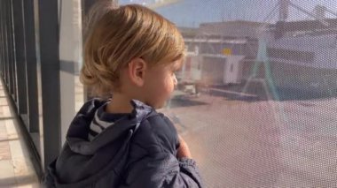 Baby boy standing by window at airport looking at planes