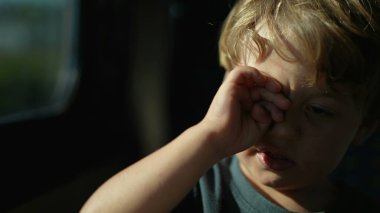 Çocuk trenle seyahat ederken gözünü ovalıyor. Yorgun çocuk, uykulu hissediyor.