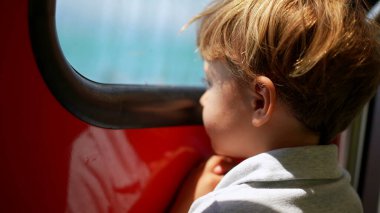 Küçük çocuk trenin penceresinden dışarı bakıyor manzaraya bakıyor.