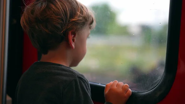 Toddler stands by train window staring outside daydreaming