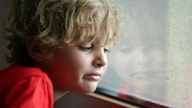 Gözü yaşlı çocuk, yağmurlu bir günde pencereden dışarı çıkmak istiyor.