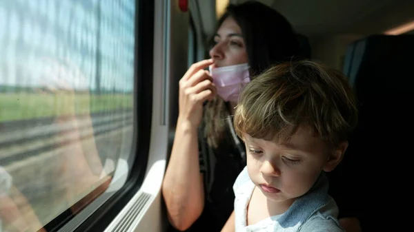 Mother putting surgical face mask while riding ktrain with toddler