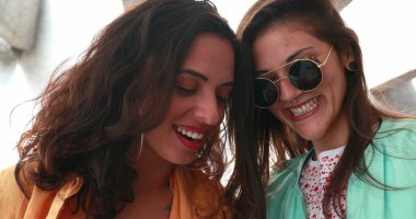 Two girls holding smartphone device, laughing and smiling to content online