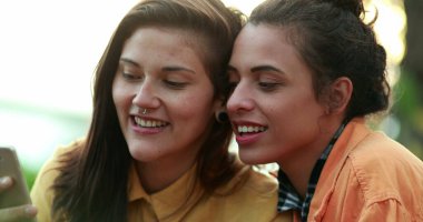 Two girls watching streaming content online. Women looking at phone screen laughing