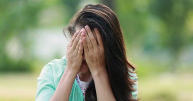 Casual millennial young woman adjusting hair rubbing face with hand outdoors at park