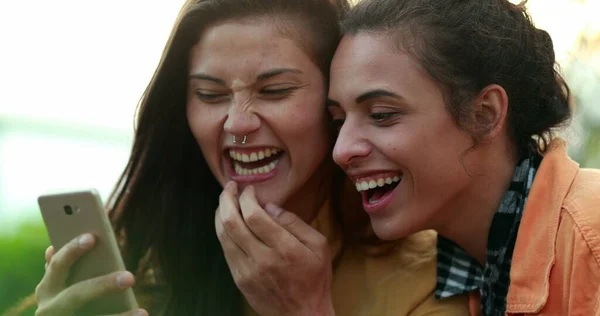 Candid young women laughing to content online using cellphone