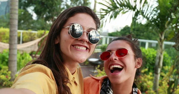 Funny girls holding camera and taking selfie of themselves while grimacing and posing