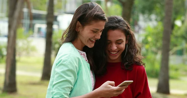 Candid two lesbian women kissing at park looking at cellphone