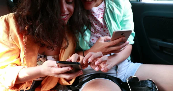 Women in backseat of car looking cellphone device, girlfriend spontaneous hiding screen from friend