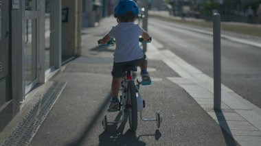 Bir çocuk şehir kaldırımında bisiklet sürüyor.