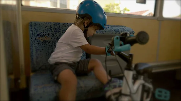 Little boy seated on public bus holding bicycle wearing helmet