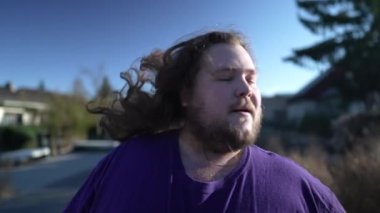 Funny Young happy man takes off the rubber band from his hair outside. An overweight person feeling free shaking head with long hair