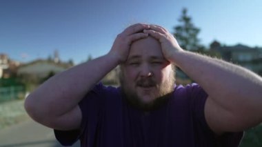 One desperate young fat man feeling upset. Overweight person feeling angry suffering from emotional problems walking outdoors. Tracking shot
