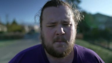 One upset young overweight man walks outside closeup face. Tracking shot of a male fat person with concerned angry expression